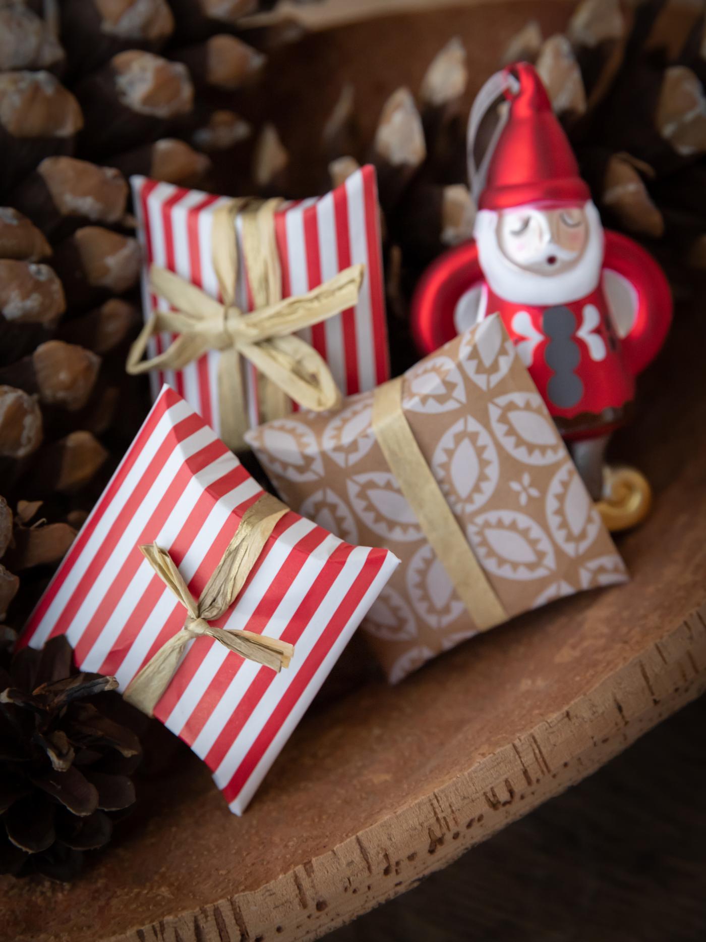 Drei kleine Geschenke neben Tannenzapfen.