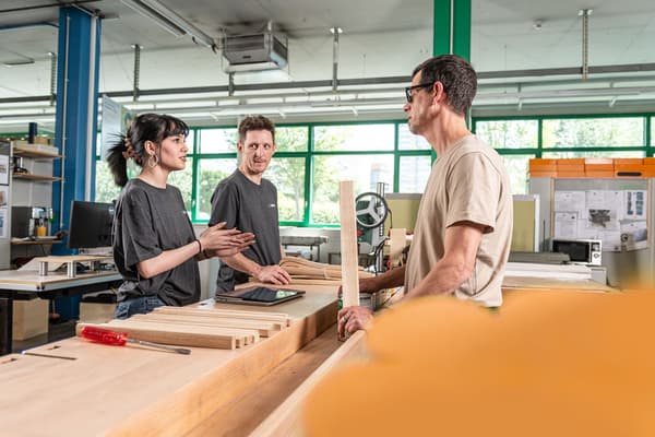 Drei Mitarbeitende des sozialen Unternehmens BAND stehen an einer Werkbank und beraten sich zusammen. 