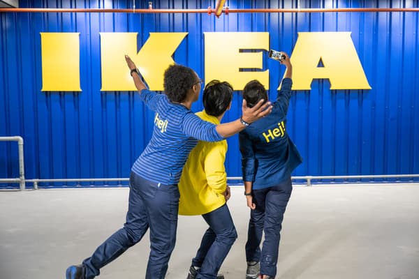 Drei Personen stehen vor einer blauen Wand mit gelbem IKEA Logo.