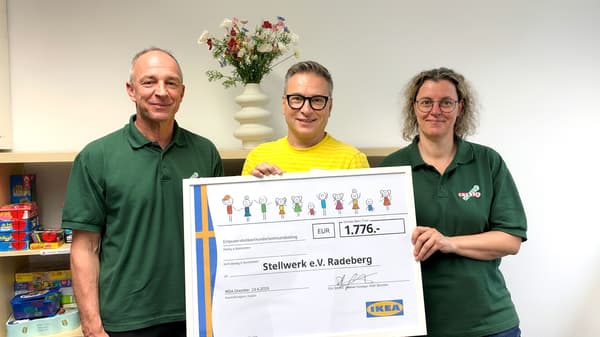 Drei Personen, zwei Männer und eine Frau stehen da und halten einen großen Scheck. Auf dem Scheck sind deutlich das IKEA-Logo, der Empfänger „Stellwerk e.V. Radeberg“ und der Betrag „EUR 1.776,-“ zu sehen. 