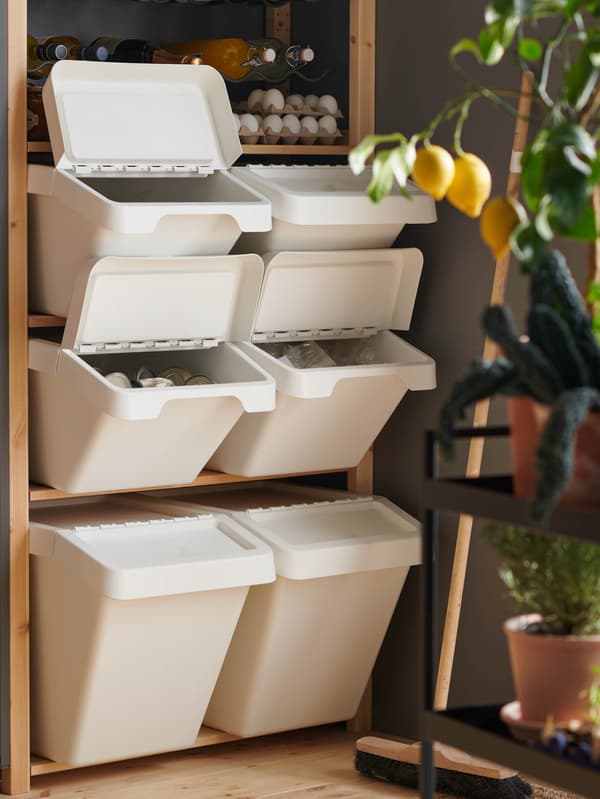 Drevené police v komore plné bielych odpadkových košov SORTERA s vytriedeným odpadom.