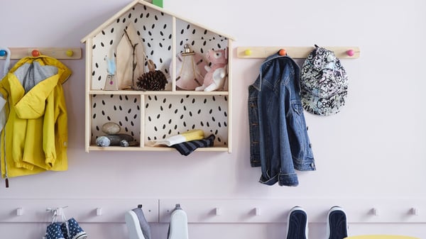 Drevený domček na hračky a háčiky s detským oblečením zaveseným na stene.