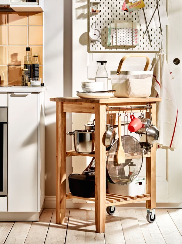 Drevený vozík BEKVÄM s hrncami, panvicami a ďalšími kuchynskými doplnkami umiestnený ako pokračovanie pracovnej dosky.