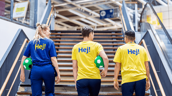 Drie IKEA medewerkers lopen de trap op. Twee daarvan hebben een groene voetbal vast.