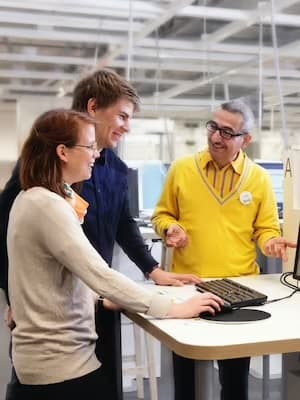 Drie mensen staan rond een computer in een kantooromgeving.