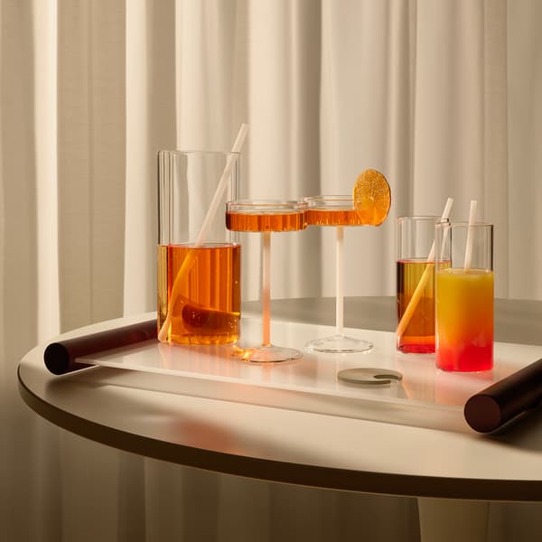 Drinkglas och vas med orange dryck står på en bricka på ett bord. 