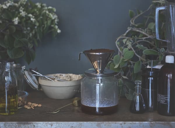 Drip coffee filtering into a glass jar on a table with other jars and ingredients.
