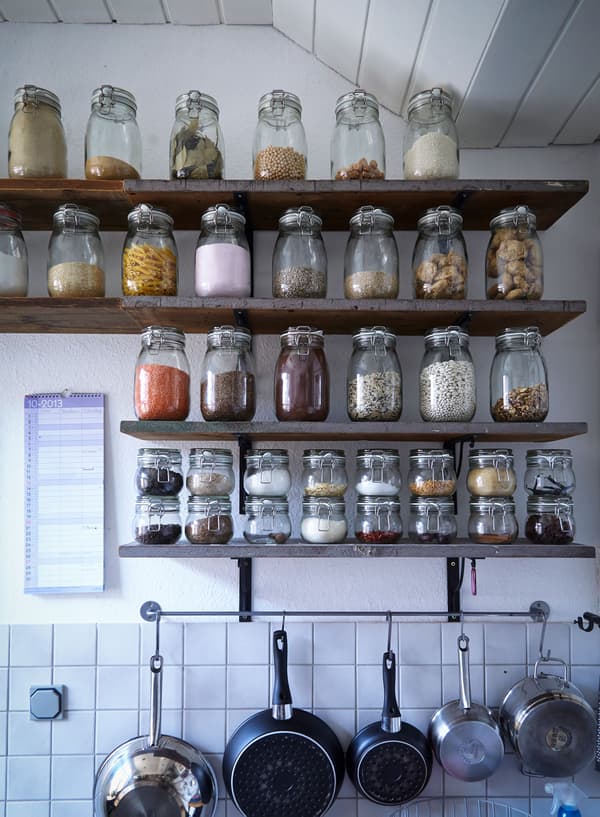 Dry ingredients are displayed (and stored) in matching jars along wooden shelves in a white kitchen.