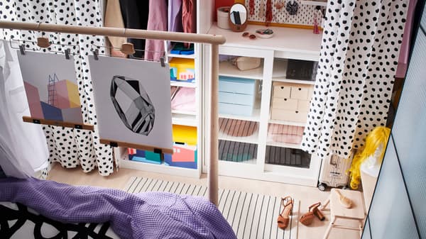 Du rangement le long d’un mur, y compris une armoire SYVDE avec portes vitrées faisant office de pièce-penderie, avec des rideaux qui servent de portes.