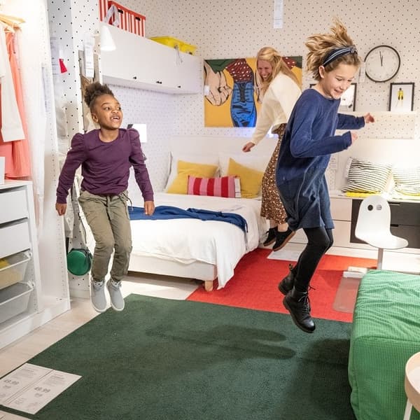 Du vaikai ir moteris šokinėja IKEA salone.