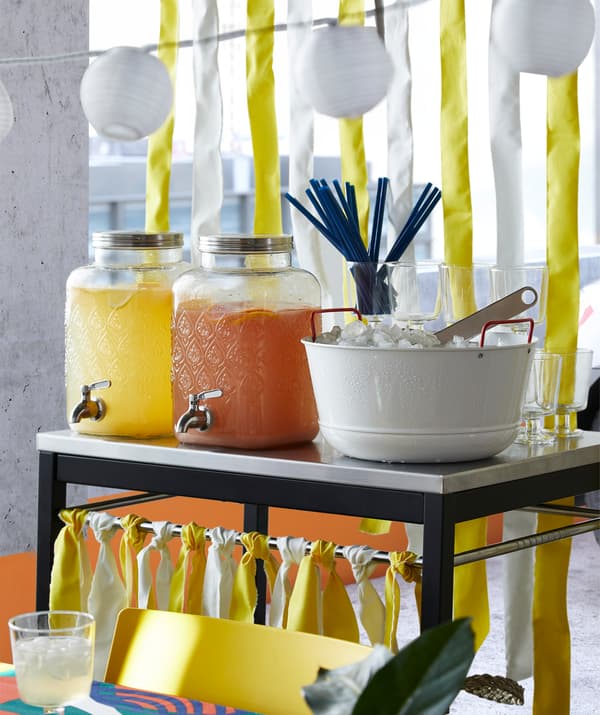 Dua balang gelas FÖRFRISKNING IKEA dengan paip yang diperbuat daripada keluli tahan karat dan diisi dengan jus buah berwarna kuning dan jingga untuk parti.