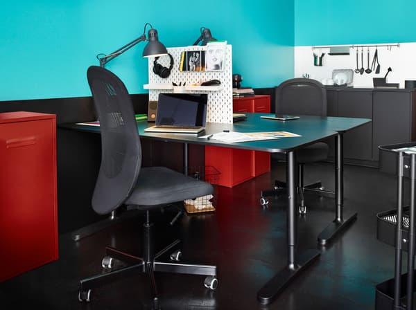 Dua meja menghadap satu sama lain dipisahkan oleh papan penyepit SKÅDIS, setiap meja dengan kerusi FINTAN, lampu kerja TERTIAL dan kabinet IVAR berwarna merah.