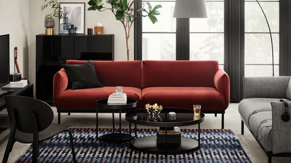 Dua sofa ÄPPLARYD, satu berwarna merah dan satu lagi kelabu, terletak di ruang tamu yang terang di sekeliling dua meja kopi berwarna hitam, dengan kerusi malas bertentangannya.
