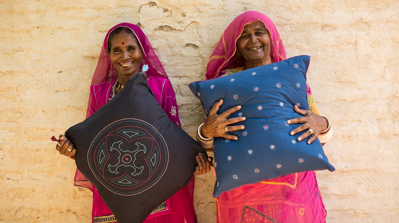 Duas artesãs, que trabalham com um empreendedor social na Índia, a segurar as almofadas artesanais que fizeram para a IKEA.