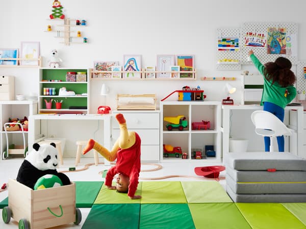 Duas crianças, uma a fazer um movimento acrobático em cima de um colchão de ginástica PLUFSIG, brincam num quarto com brinquedos, arrumação e desenhos nas paredes.