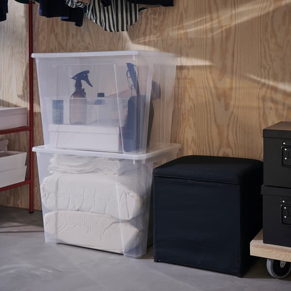 Due contenitori trasparenti SAMLA impilati sul pavimento, accanto a un poggiapiedi nero con contenitore - IKEA