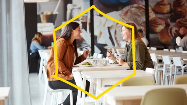 Due donne sorridenti sedute una di fronte all'altra in un ristorante IKEA mentre mangiano.