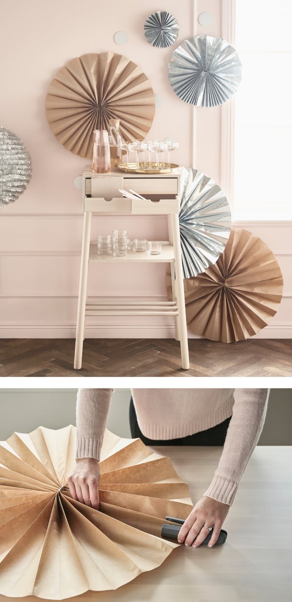 Due immagini in cui una persona crea con carta regalo GIVANDE una composizione di coccarde natalizie e una in cui queste composizioni sono adagiate su una parete rosa. Accanto alle composizioni una scaletta su cui sono adagiati dei bicchieri sui diversi ripiani.
