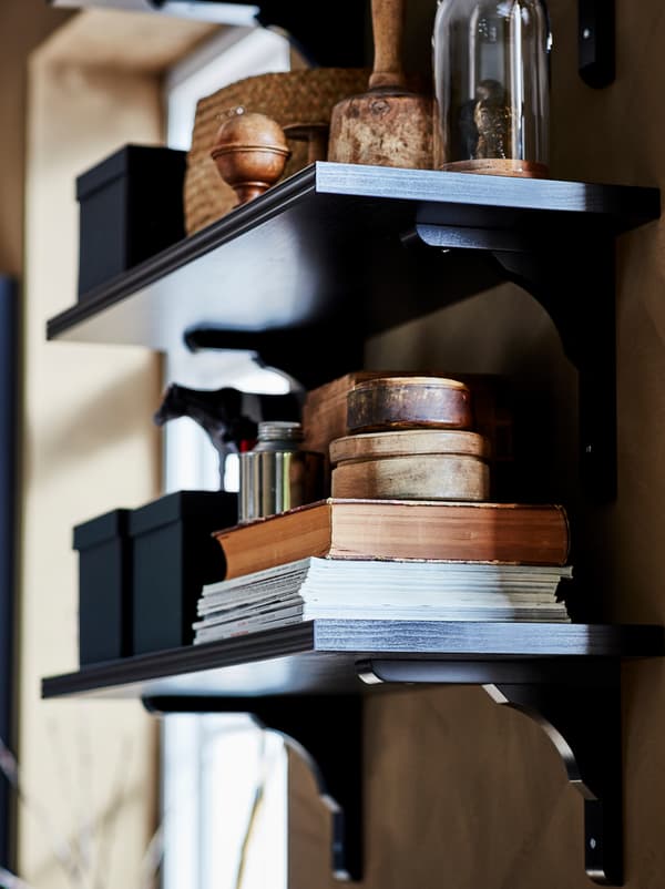 Due mensole e staffe BERGSHULT/RAMSHULT marrone/nero con libri, scatole e oggetti decorativi.