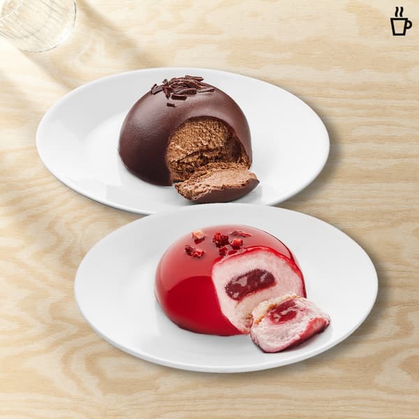 Due mousse una al cioccolato e una ai lamponi in un piatto bianco su un tavolo legno chiaro