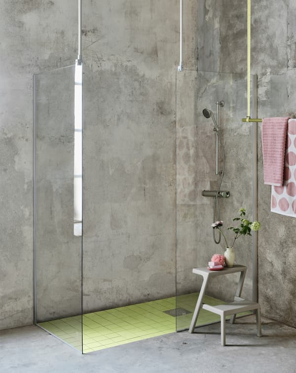 Due pareti doccia OPPEJEN utilizzate per creare una spaziosa cabina doccia in un bagno di cemento grigio con accessori rosa.