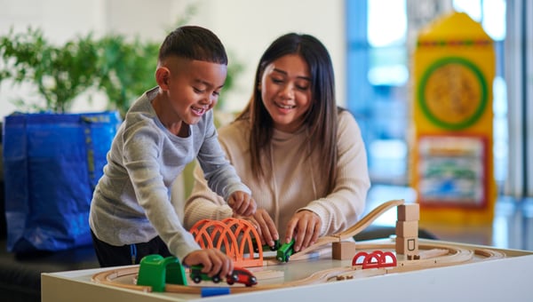 Due persone giocano su un tavolo di casa con una pista e macchinine LILLABO.  