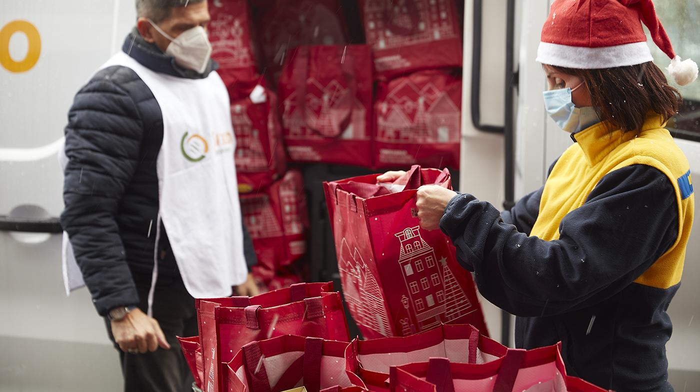 Due persone intente a preparare dei sacchetti alimentari e a caricarli dal retro di un furgone aperto.