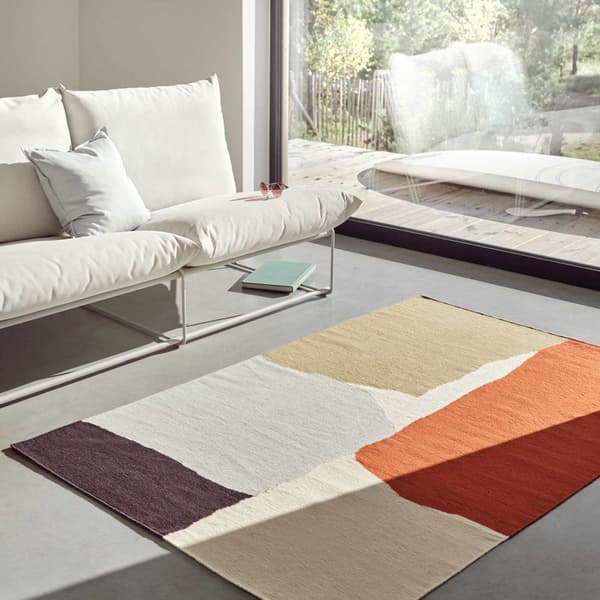 Due poltrone bianche e un tappeto decorato con una fantasia di macchie di diversi colori sono illumunati dalla luce del sole. 