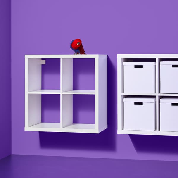 Due scaffali KALLAX bianchi appesi a una parete viola; uno è vuoto, l'altro contiene delle scatole bianche sui ripiani.