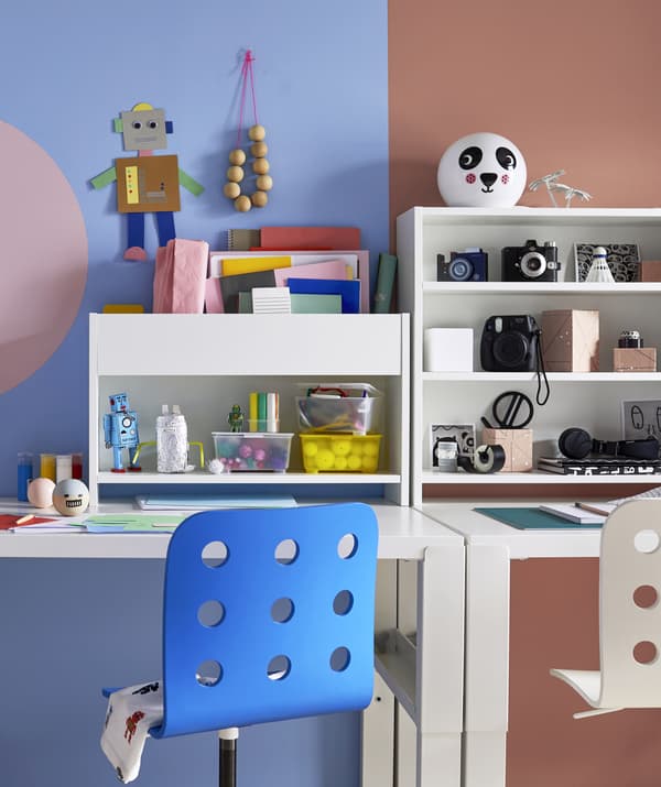 Due scrivanie affiancate davanti a una parete dipinta in lilla e color corallo.