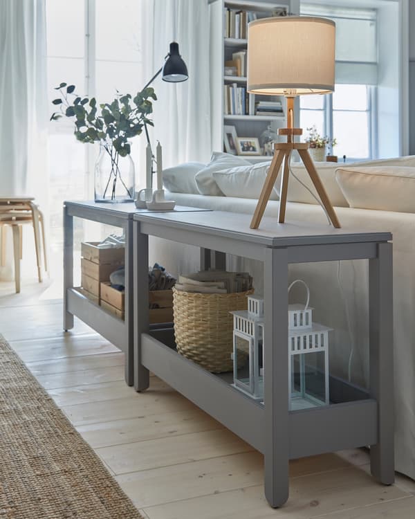 Due tavoli consolle grigi alle spalle di un divano, usati come divisori decorativi, con due lampade da tavolo – IKEA