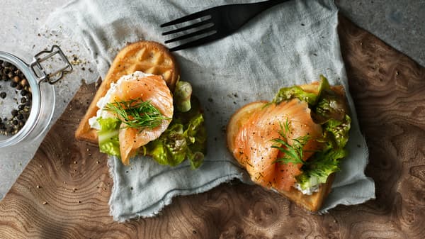 Due waffle VÅFFLOR a forma di cuore decorati con salmone, formaggio spalmabile, aneto e lattuga su un pezzo di stoffa, accanto a una forchetta - IKEA