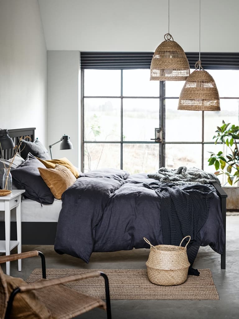 Dunkles Bett mit blauer Bettwäsche und einem weissen Nachttisch.