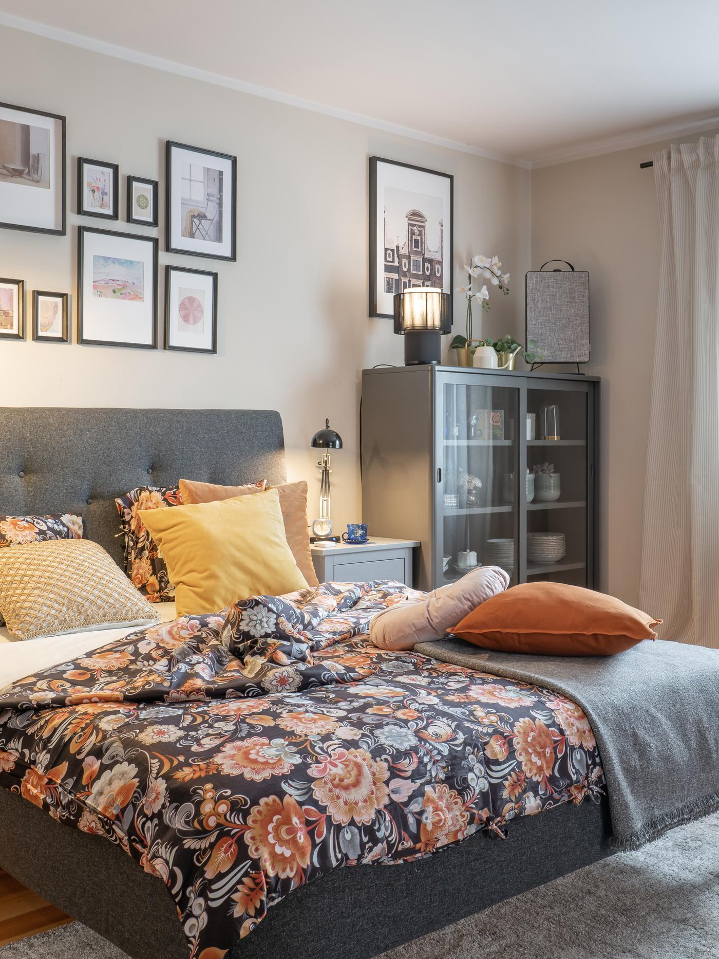 Duża, bezowa sypialnia z łóżkiem z kwiecistą pościelą.