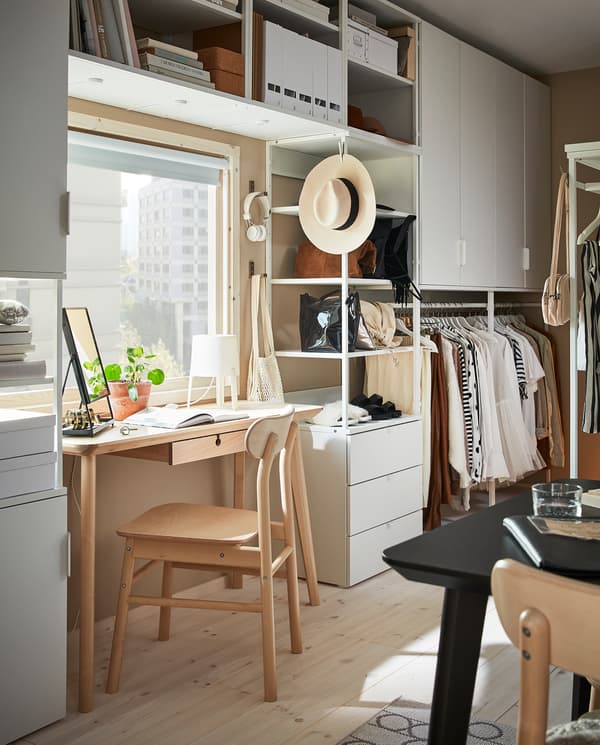 Duża kombinacja do przechowywania PLATSA zamontowana na ścianie wokół okna, przy którym idealnie mieści się biurko.