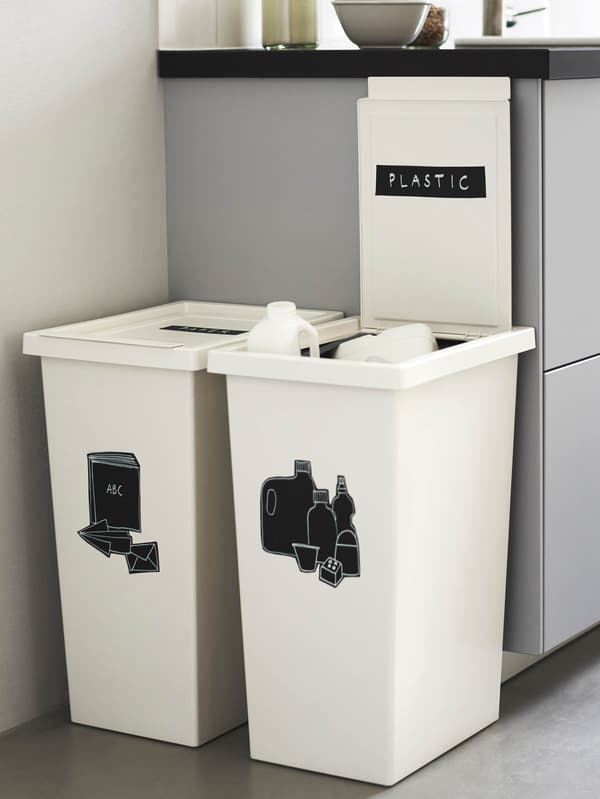 Dva biele koše FILUR s čiernymi samolepkami označujúcimi obsah stoja vedľa svetlosivej kuchynskej linky.