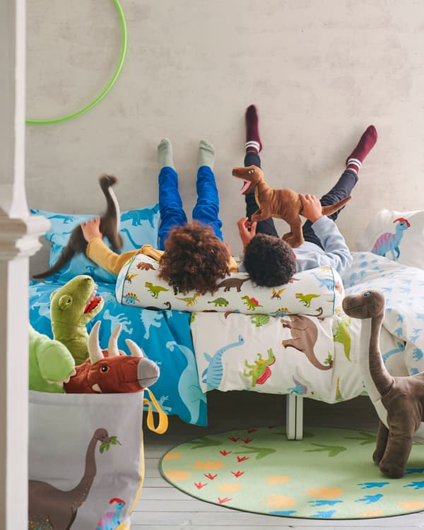 Dva chlapci leží na posteli s nohama opřenýma o zeď, pod sebou povlečení s obrázky dinosaurů ze série JÄTTELIK 