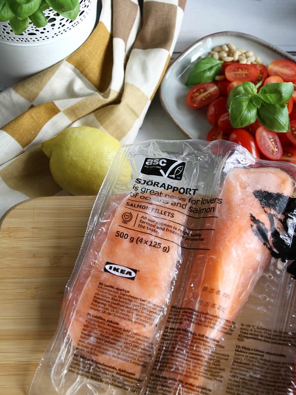 Dva filety lososa SJÖRAPPORT sú položené na doske STOLHET, vzadu je citrón a tanier GLADELIG s nakrájanými cherry paradajkami a bazalkou.