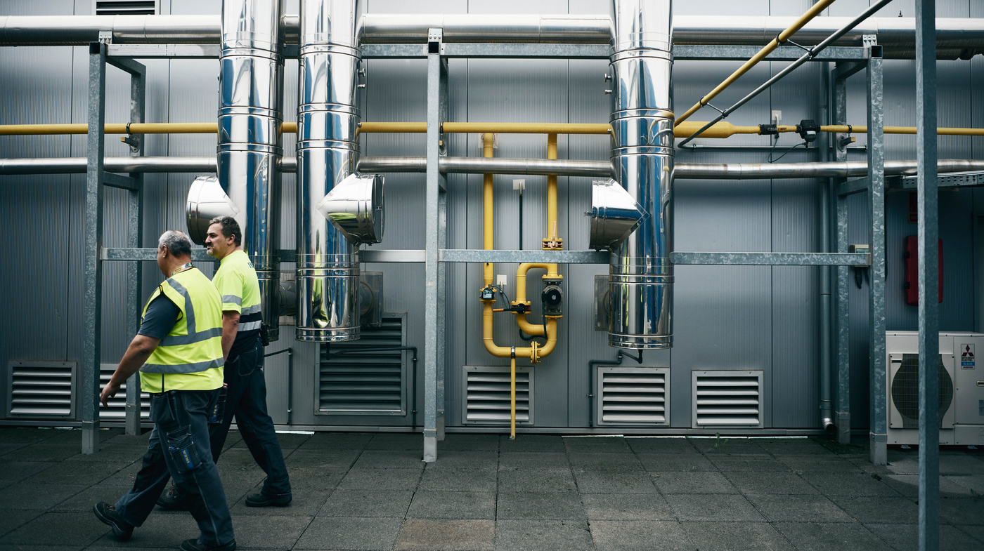 Dva muži v IKEA uniformách jdou před před recyklačním centrem, za nimi trubky nerezové a žluté