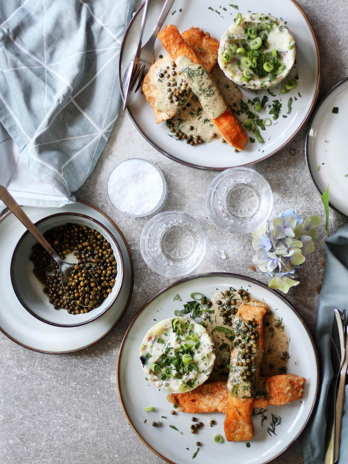 Dva talíře GLADELIG s porcí lososa se šťouchanými bramborami a pepřovo-sýrovou omáčkou, vedle dezertního talíře a misky GLADELIG s naloženým zeleným pepřem.