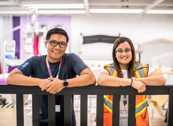 Dva zaměstnanci IKEA se zaměstnaneckou kartou na krku se opírají o dřevěné zábradlí.
