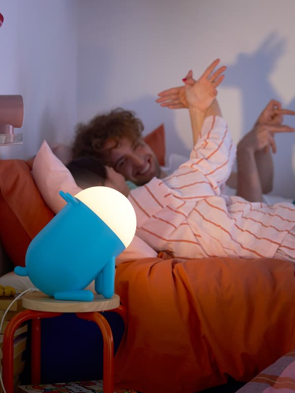 Dvaja mladí ľudia tvoria tieňové figúrky zvierat pomocou rúk a modrej stolovej lampy v tvare psa GREJSIMOJS.