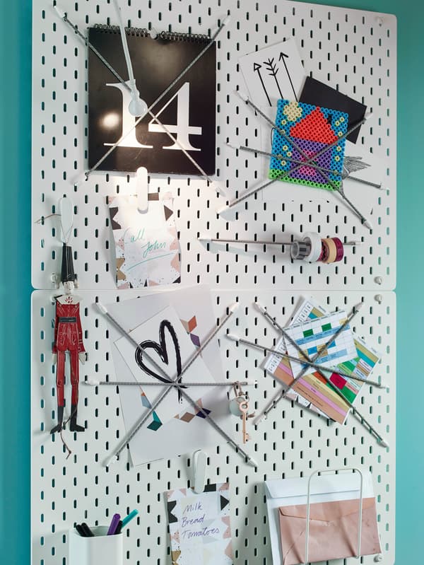 Dve biele dierkované dosky SKÅDIS s pružnými lankami, za ktorými sú obrázky a kotúče lepeniek.