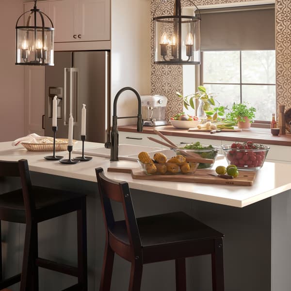 Dve crne/staklene lampe u obliku cilindara, bela kuhinjska vrata i fioke, crna kombinovana slavina i sive roletne.