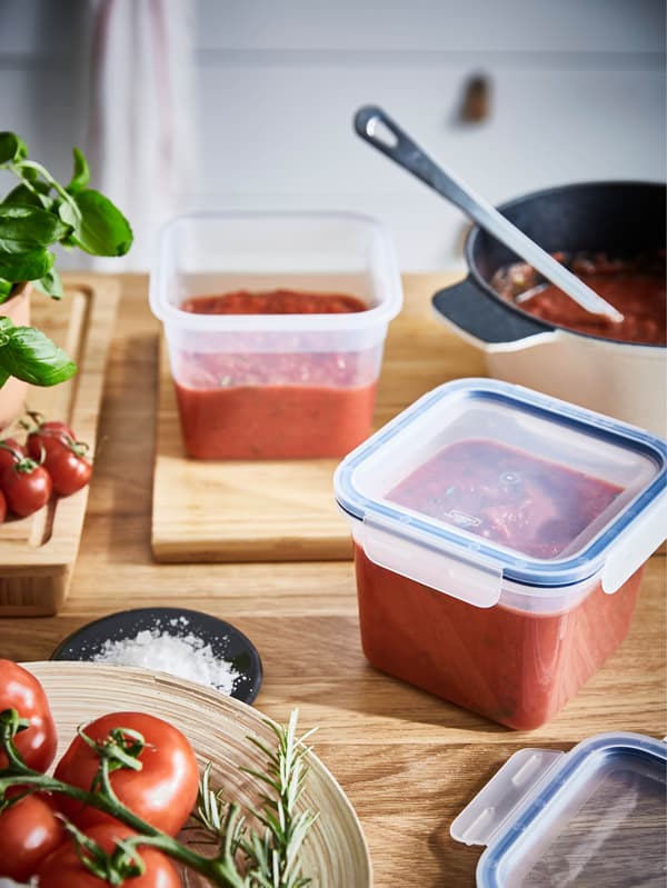 Dvě čtvercové dózy IKEA 365+ 1,4 l plné rajčatového pyré stojí na dřevěné pracovní desce.