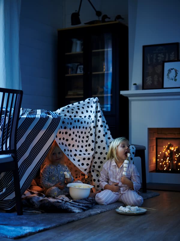 Dve dievčatá jedia penové cukríky bunkri vyrobenom z látky METTALISE a SKÄGGÖRT omotané okolo stola EKEDALEN.