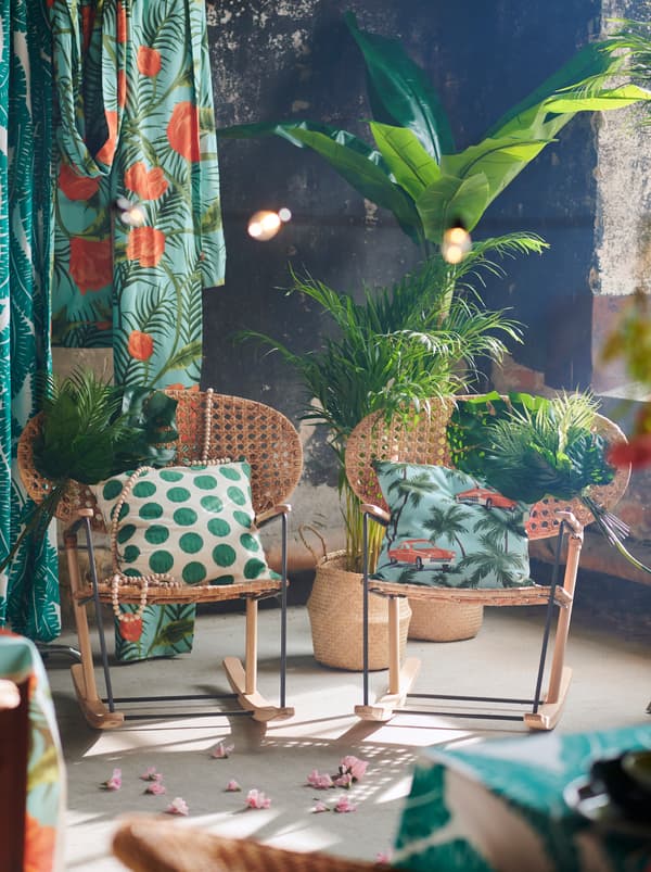 Dve ozdobené hojdacie kreslá GRÖNADAL vedľa seba s farebnými textíliami, tropickými rastlinami a kvetmi okolo.