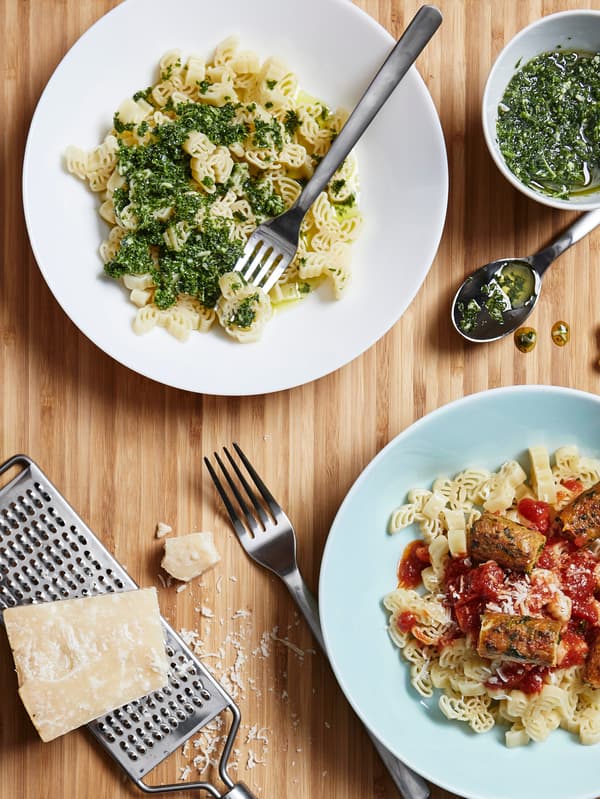 Dve porcie cestovín v tvare losích hlavičiek BÄSTISAR, jedna s bazalkovým pestom, druhá so zeleninovými párkami REFRÄNG a s kečupom.