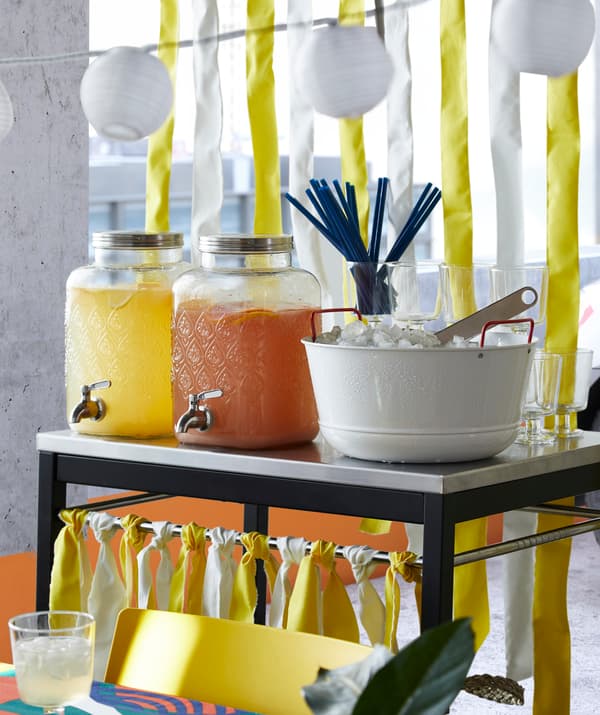 Dve sklenené dózy IKEA FÖRFRISKNING s kohútikom z nehrdzavejúcej ocele naplnené ovocnými džúsmi na oslavu.