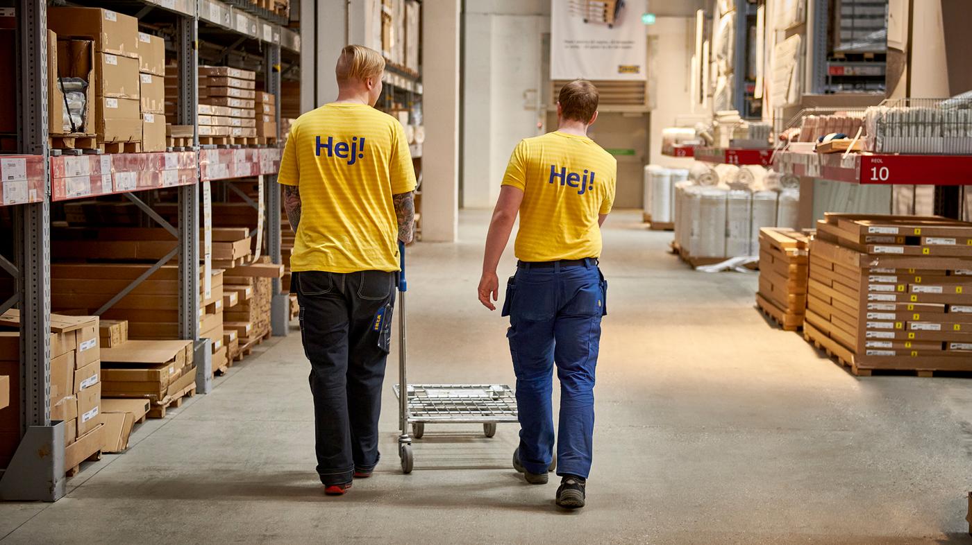 Двоє працівників магазину ІКЕА рухаються повз полиці з товарами та штовхають візок